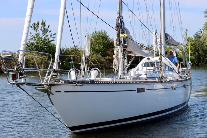 Een witte zeilboot met een blauwe streep op de romp vaart op het water, met een man aan het roer. — RJ 140