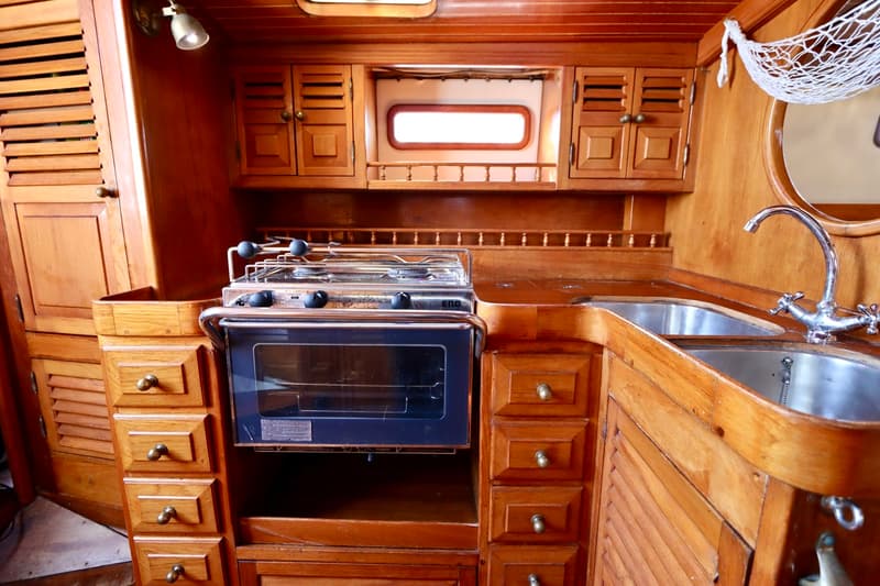 Een houten kombuis met een fornuis, oven, dubbele spoelbak en diverse kasten en lades.