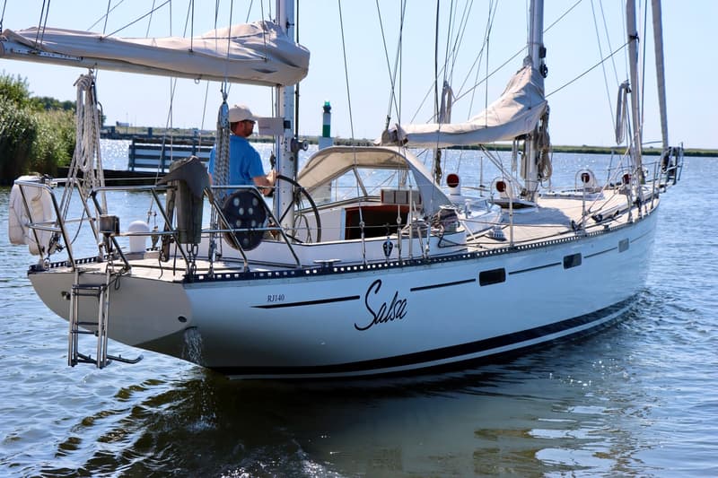 Een witte zeilboot met de naam "Salsa" en registratienummer "RJ140" vaart op het water, met een persoon aan het roer.
