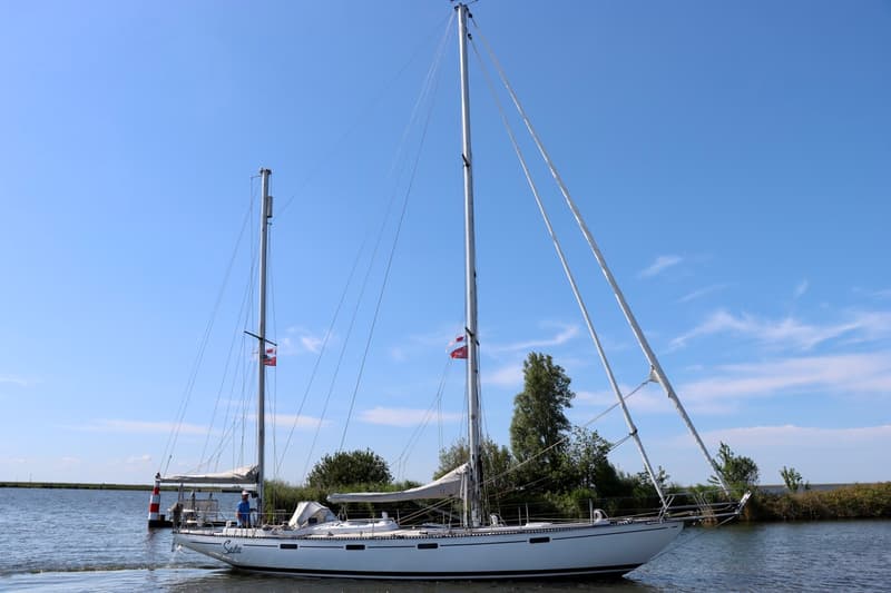 Een witte zeilboot met twee masten en de naam "Saba" op de boeg vaart op een waterweg. — RJ 140