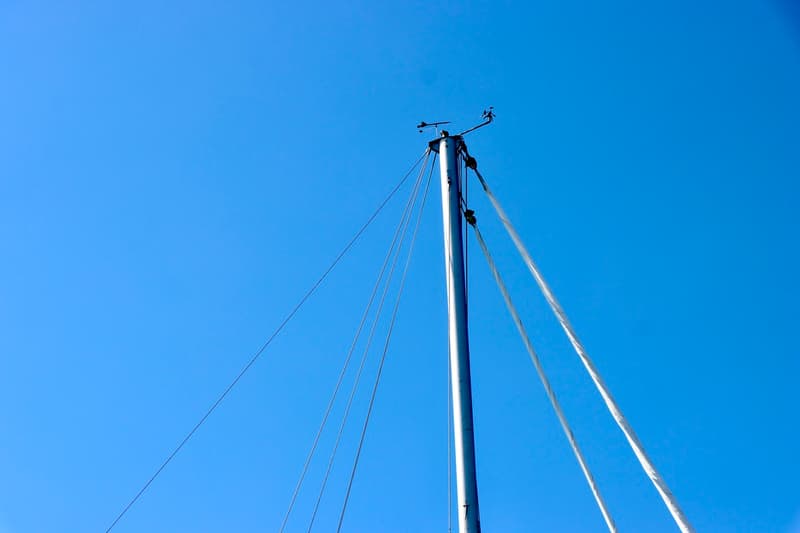 Een mast van een zeilboot met een windvaan en windmeter bovenaan, tegen een helderblauwe lucht. — RJ 140