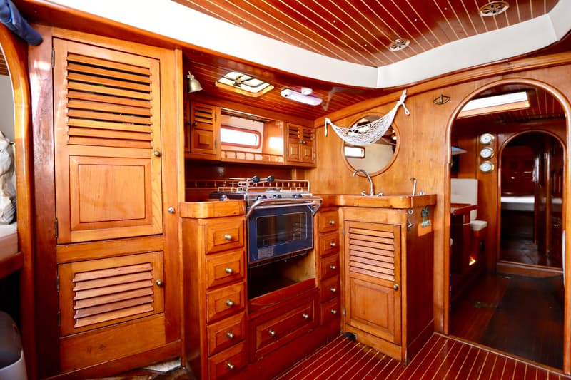 Een houten bootinterieur met een kombuis, inclusief een fornuis met oven, een gootsteen en diverse kasten.