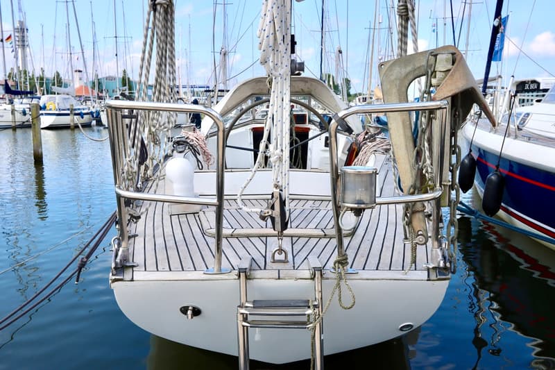 De achtersteven van een zeilboot met een houten dek, een zwemtrap en een anker, liggend in een haven. — RJ 140