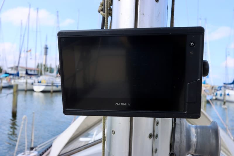 Een zwart Garmin-scherm is gemonteerd op een mast, met een jachthaven op de achtergrond.