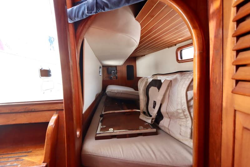 De foto toont een interieur van een boot met houten afwerking, kussens en een raam dat uitzicht biedt op een andere boot.