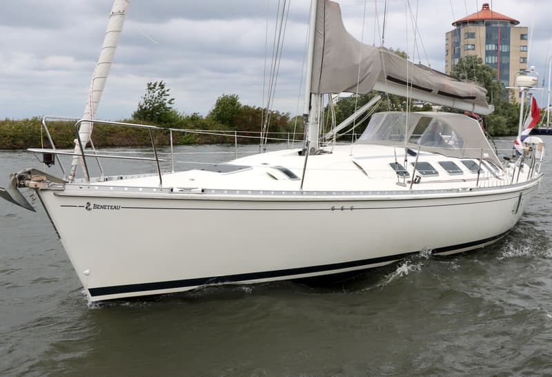 Een witte zeilboot met de naam "BENETEAU" op de boeg vaart op water met een gebouw op de achtergrond. — Beneteau First 41S5