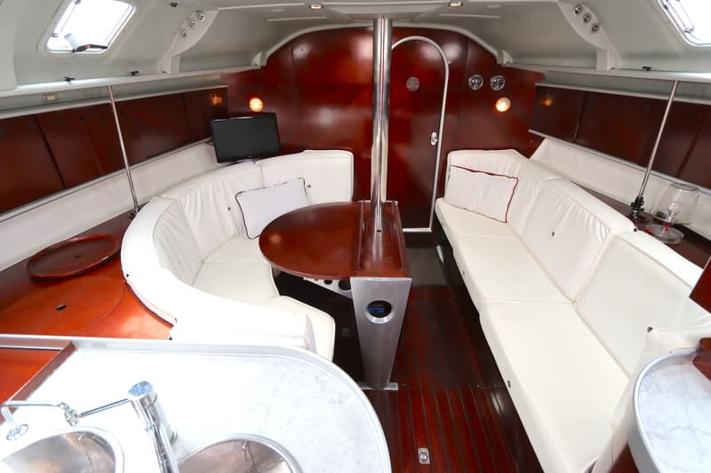 De foto toont het interieur van een boot met een zithoek, een tafel, een televisie en een gootsteen. — Beneteau First 41S5