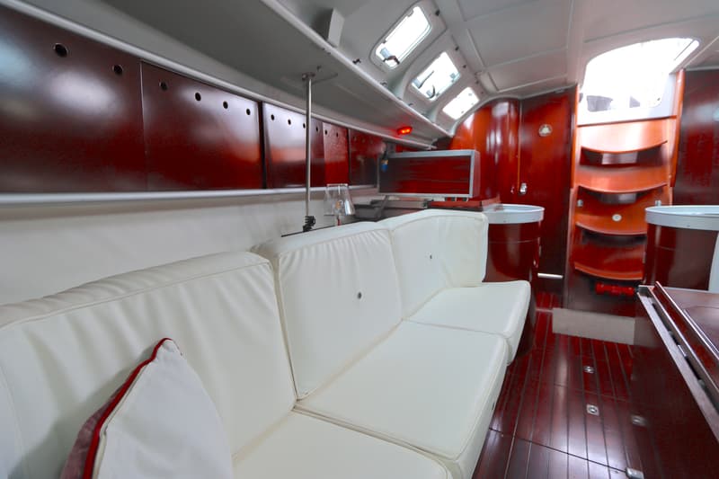 De kajuit van een boot met witte banken, rode wanden en een houten vloer is zichtbaar. — Beneteau First 41S5