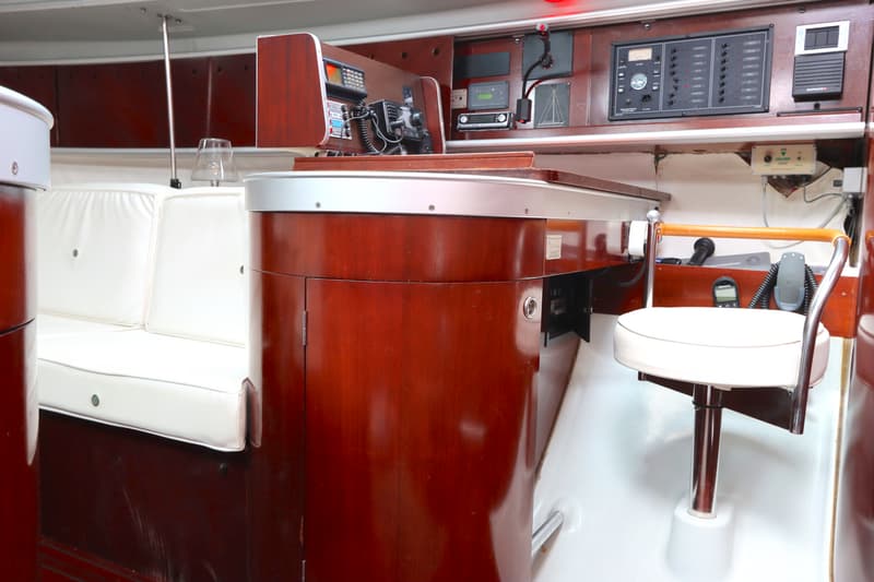 De foto toont het interieur van een boot met een houten tafel, witte banken en een draaibare stoel. — Beneteau First 41S5