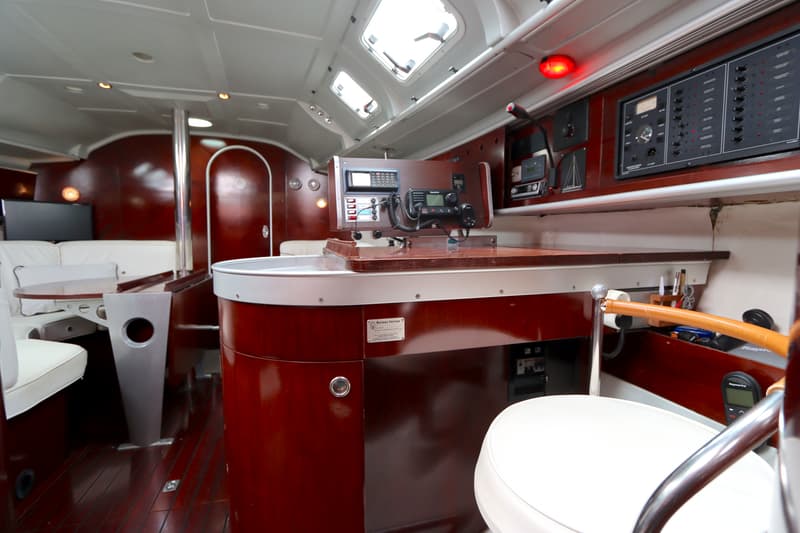 De foto toont het interieur van een boot met een houten afwerking, een navigatiehoek en een zithoek met witte kussens.