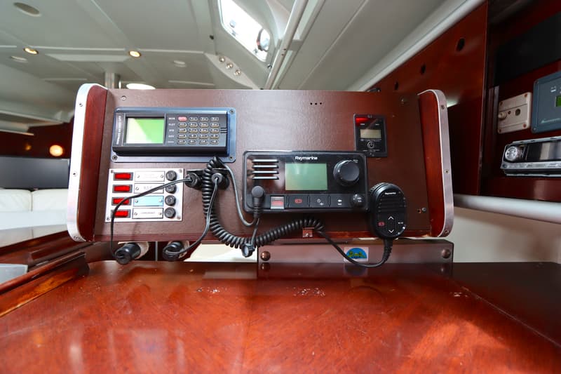 Een houten paneel met diverse navigatie- en communicatieapparatuur, waaronder een Raymarine-radio en een GPS-ontvanger.