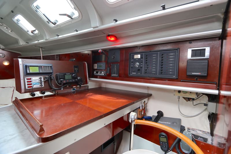 De foto toont een interieur van een boot met een houten tafel, diverse navigatie- en communicatieapparatuur, en een…