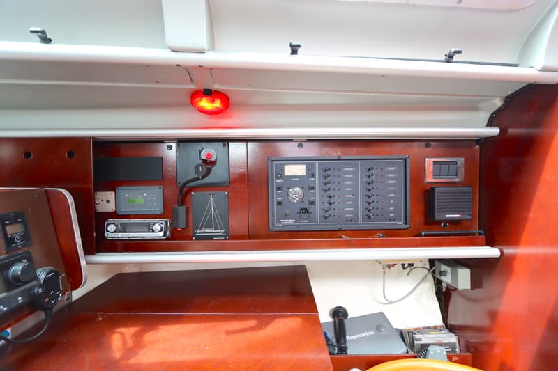 Een interieur van een boot met een houten dashboard, diverse meters, schakelaars, een radio en een rood licht.