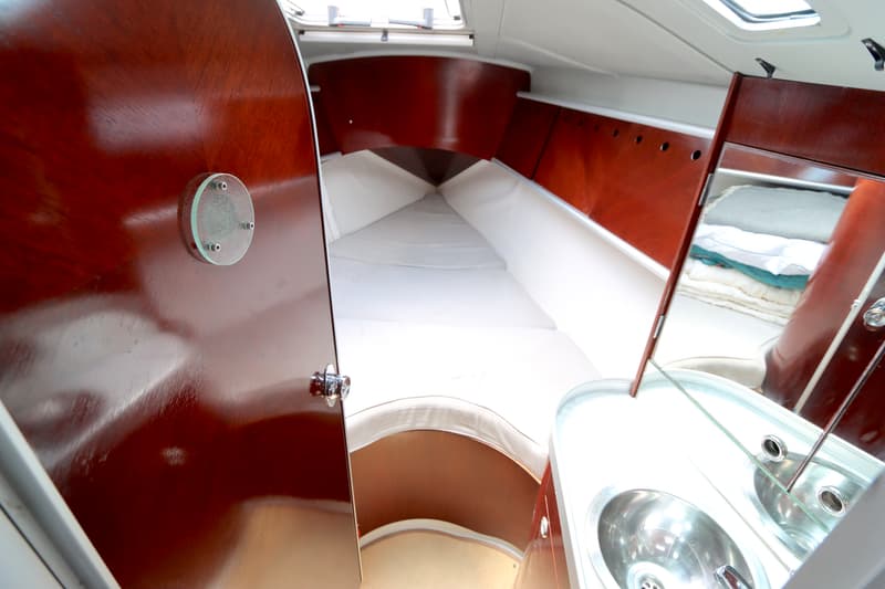 De foto toont een interieur van een boot met een bed in de boeg, een wastafel met spiegel en houten panelen.