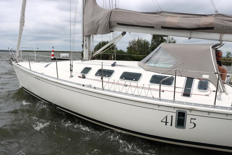 Een witte zeilboot met grijze zeilen en een grijze buiskap vaart op het water, met een persoon zichtbaar onder de buiskap.