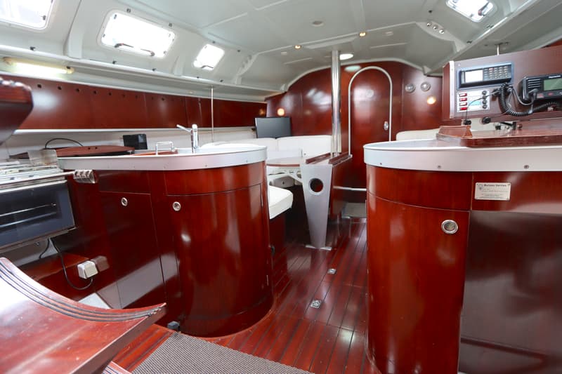 De foto toont het interieur van een boot met een houten vloer, donkerhouten meubels, een kombuis en een navigatiehoek.