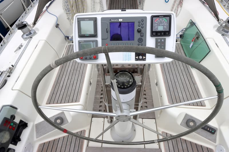 Een stuurwiel met instrumentenpaneel, kompas en houten dek op een boot. — Beneteau First 41S5