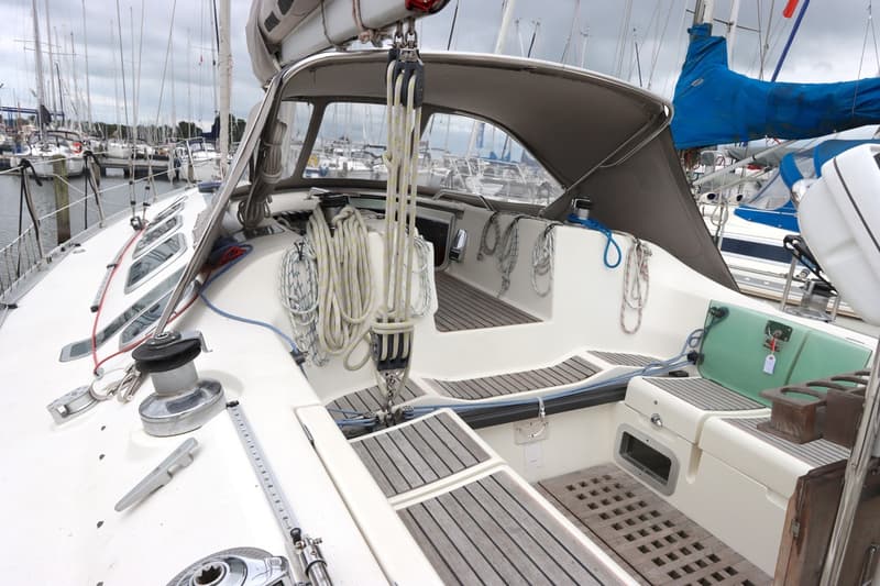 Een bovenaanzicht van de kuip van een zeilboot met touwen, lieren en een buiskap, omringd door andere boten in een haven.