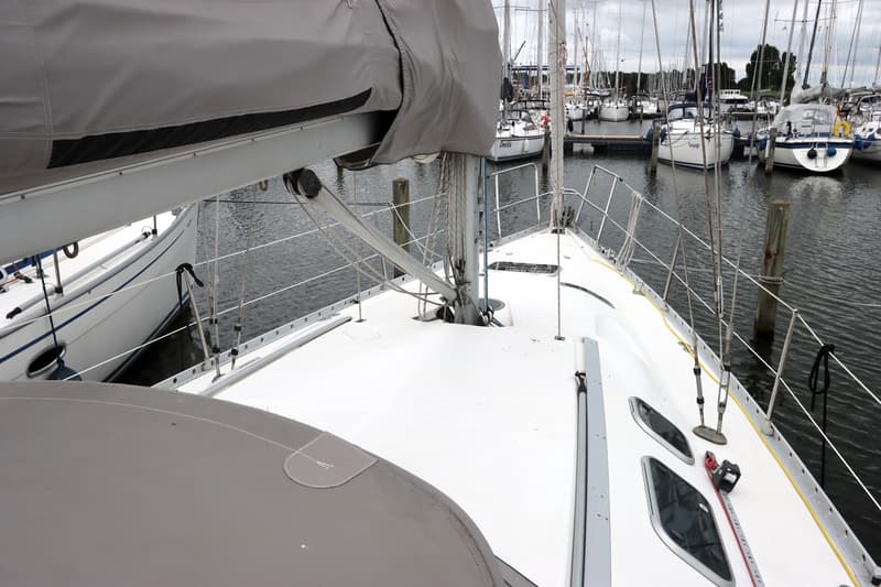 Een wit zeiljacht met een grijze zeilhoes ligt aangemeerd in een haven vol met andere zeilboten.