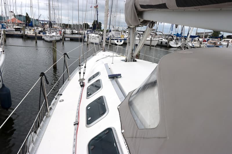 Een bovenaanzicht van het dek van een zeilboot met een grijze buiskap, omringd door andere zeilboten in een haven.