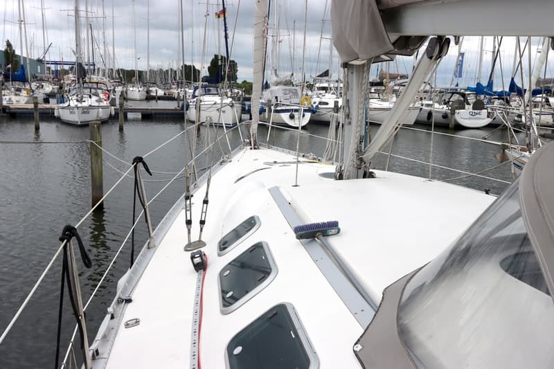 Een bovenaanzicht van het dek van een zeilboot met een meetlint en een borstel, omringd door andere zeilboten in een haven.