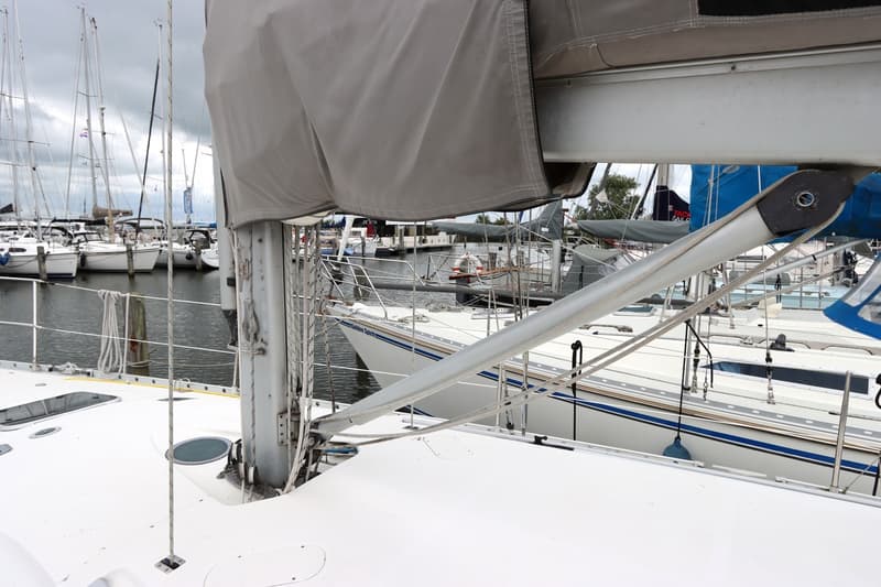 Een close-up van een zeilboot in een haven, met de mast, giek en een grijze zeilhoes prominent in beeld.