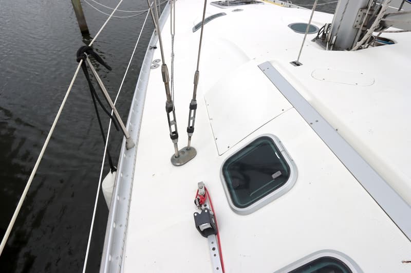 Een bovenaanzicht van het witte dek van een zeilboot met twee patrijspoorten, een stootwil en een deel van de mast.