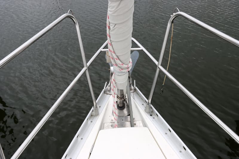 De boeg van een witte zeilboot met een opgerold zeil en roestvrijstalen reling, boven donker water. — Beneteau First 41S5