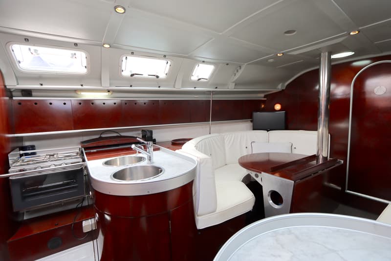 De foto toont een kajuit met een kombuis, een zithoek met witte kussens, een tafel en een televisie. — Beneteau First 41S5