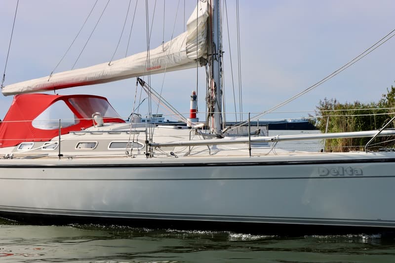 Een witte zeilboot met de naam "Delta" op de romp, een rode buiskap en een opgerold zeil aan de giek. — Dehler 36 CWS