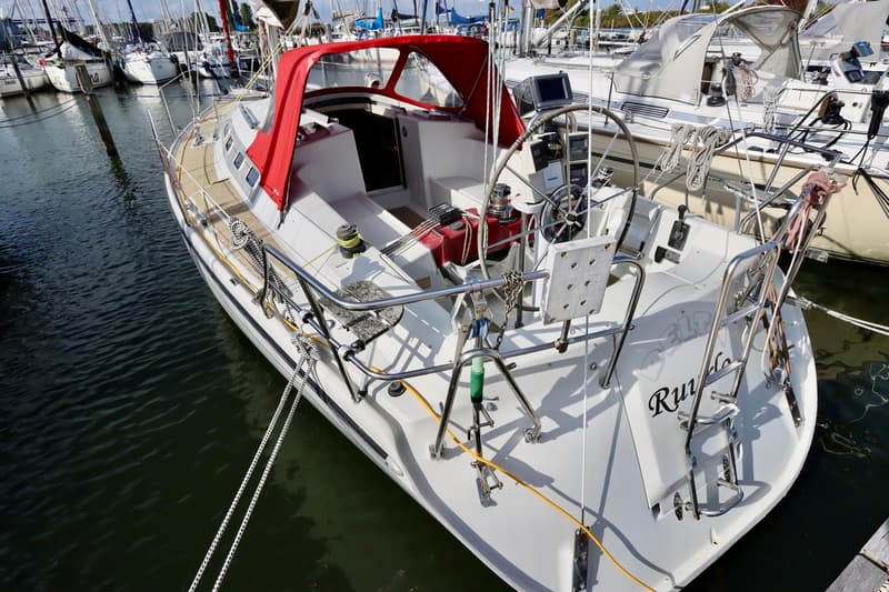 Een witte zeilboot met een rode buiskap en de naam "Rurudo" op de spiegel ligt afgemeerd in een jachthaven. — Dehler 36 CWS