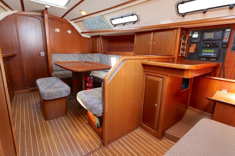De houten kajuit toont een zithoek met tafel, een navigatiehoek en een brandblusser op de vloer. — Bavaria 35 Holiday
