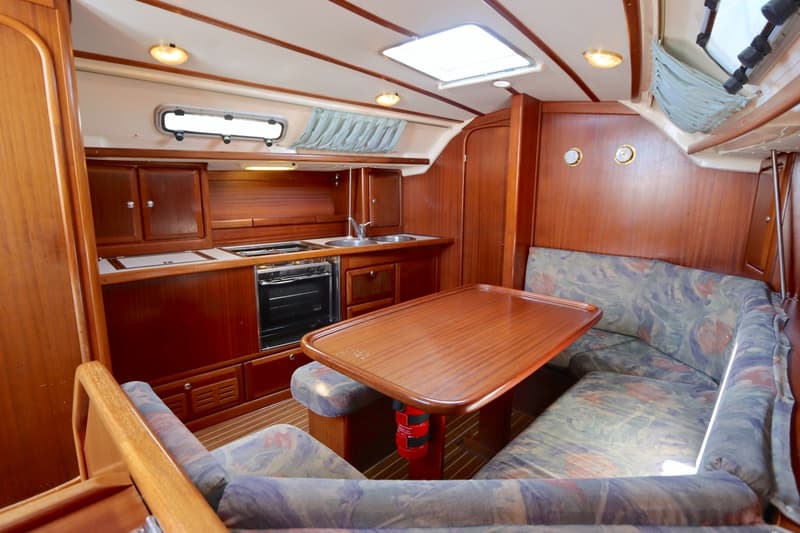 De foto toont een houten interieur van een boot met een kombuis, zithoek met kussens, tafel en een brandblusser.