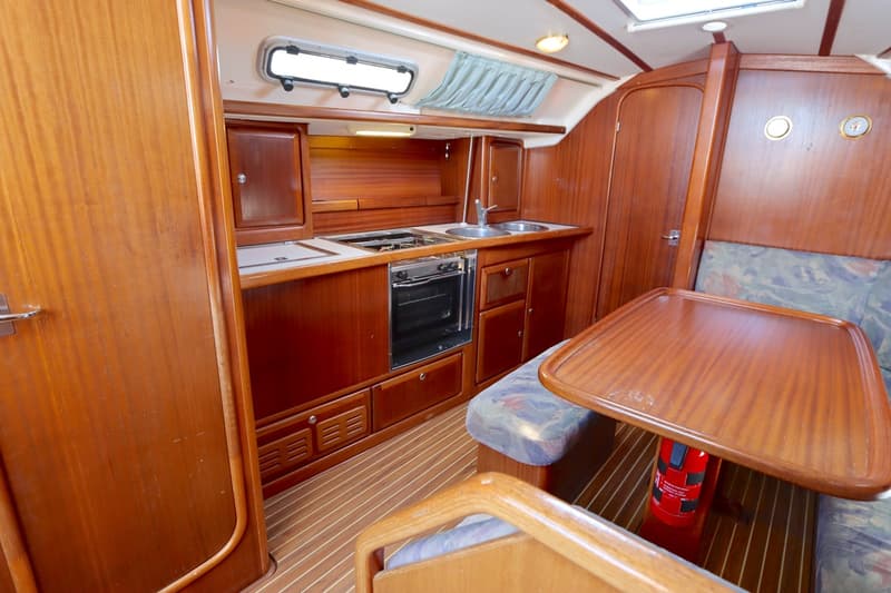 De foto toont een houten bootinterieur met een kombuis, een eettafel met banken en een brandblusser op de vloer.
