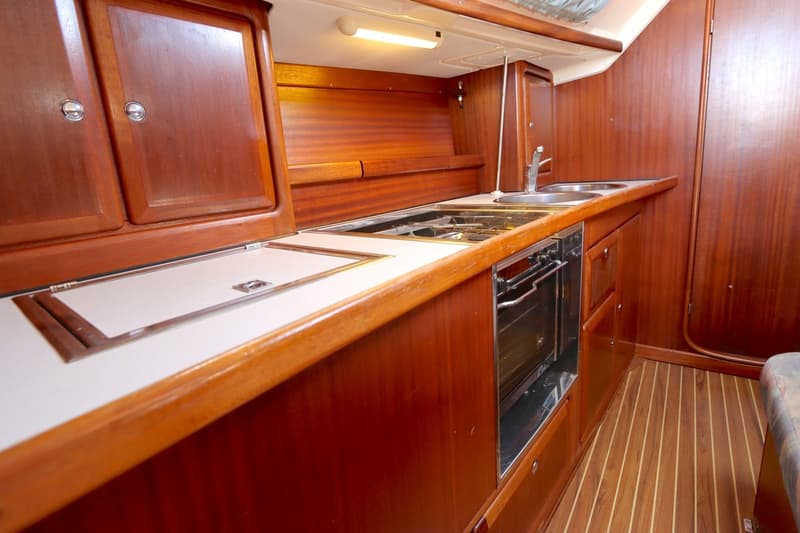 De foto toont een scheepskeuken met houten kasten, een aanrecht, een fornuis met oven en een dubbele spoelbak.