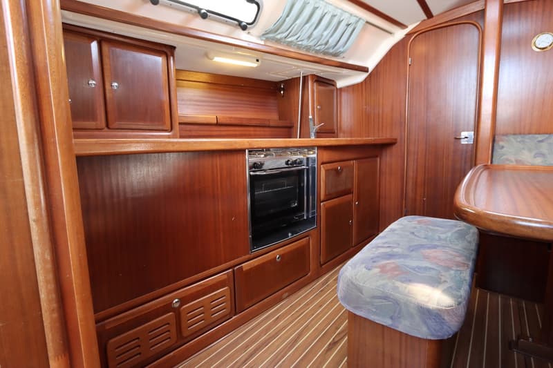 Een houten scheepsinterieur met kombuis, fornuis met oven, spoelbak, kasten, een bankje en een tafel.