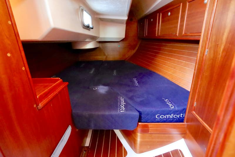 Een bootkajuit met een blauw matras, houten betimmering, kasten en een klein raam is zichtbaar.
