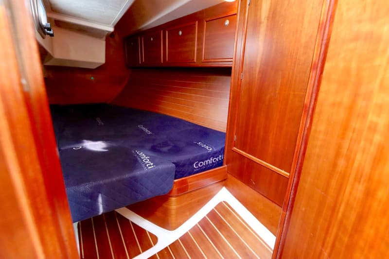 Een kajuit met een donkerblauw matras, houten wanden, houten vloer met witte strepen en houten kasten is zichtbaar.