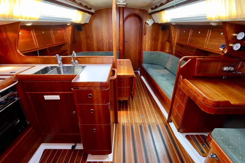 De kajuit van een boot is zichtbaar, met een houten interieur, een kombuis met dubbele spoelbak en een zithoek met groene…