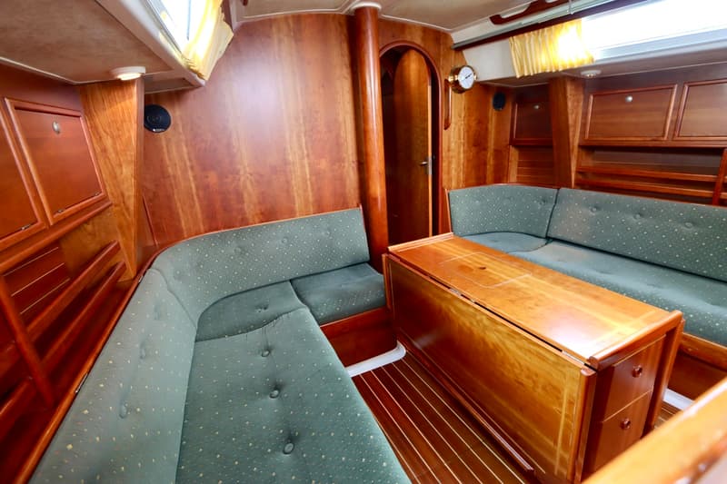 De kajuit toont een houten interieur met groene gestoffeerde banken, een houten klaptafel en een doorgang. — Winner 1120
