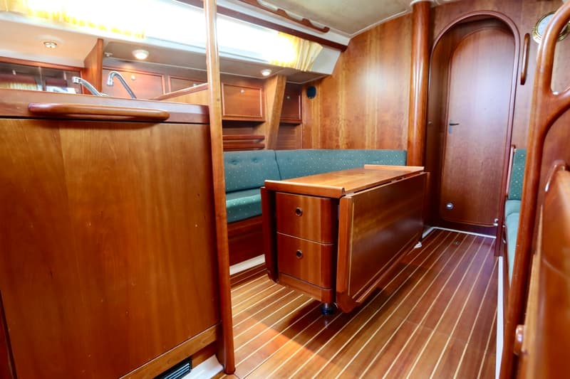 Een houten interieur met gestreepte vloer, groene banken, een inklapbare tafel met lades, een kombuis en een deur.