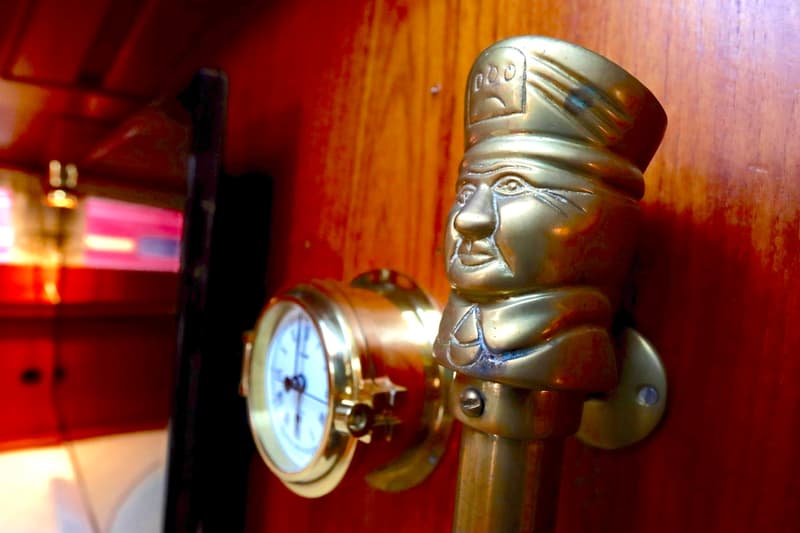 Een messingkleurig decoratief hoofd en een klok met witte wijzerplaat zijn gemonteerd op een houten wand.