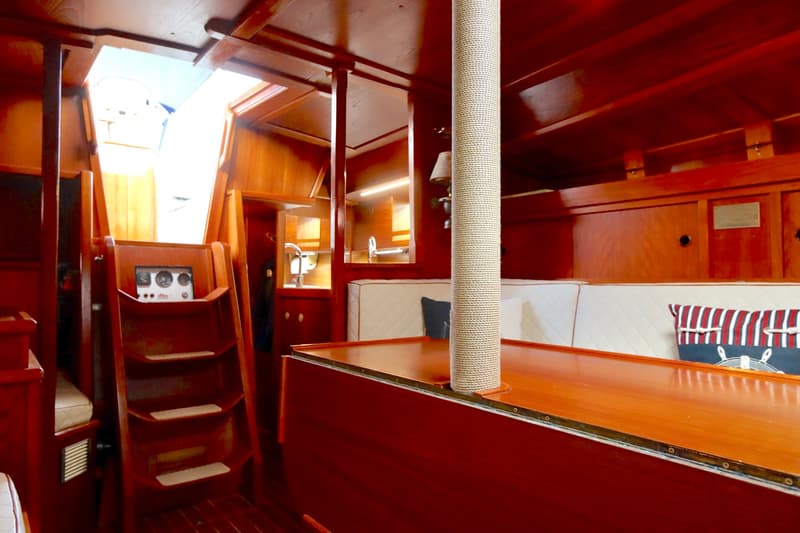 De kajuit van een boot is zichtbaar, met een houten interieur, een trap, een instrumentenpaneel, een kombuis en zitbanken.