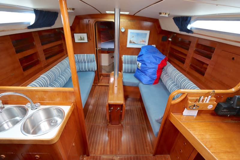 De kajuit van een boot toont een houten interieur met twee banken met blauwe kussens, een gootsteen en een tafel. — Moody 376
