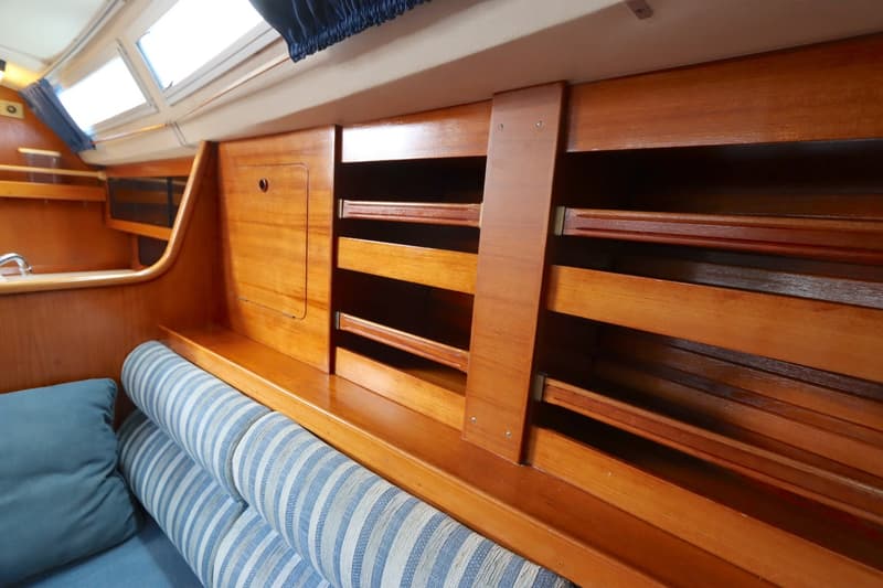 De kajuit toont een houten interieur met een bank met gestreepte kussens, opbergvakken en ramen met gordijnen. — Moody 376