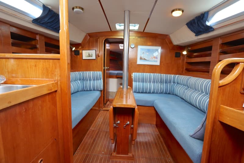De kajuit van een boot toont een houten interieur met blauwe banken, een inklapbare tafel en een maststeun. — Moody 376