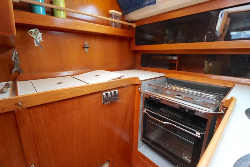 Een scheepskeuken met houten betimmering, een gasfornuis met oven, een werkblad, opbergruimte en een flesopener.