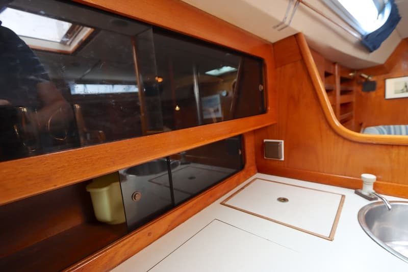 De foto toont een houten interieur met schuifdeuren van donker glas, een aanrechtblad met spoelbak en een luik.