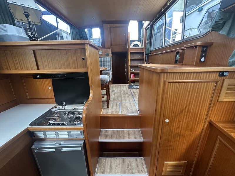 Een interieur van een boot met een kombuis aan de linkerkant, een trap in het midden en een doorgang naar achteren.