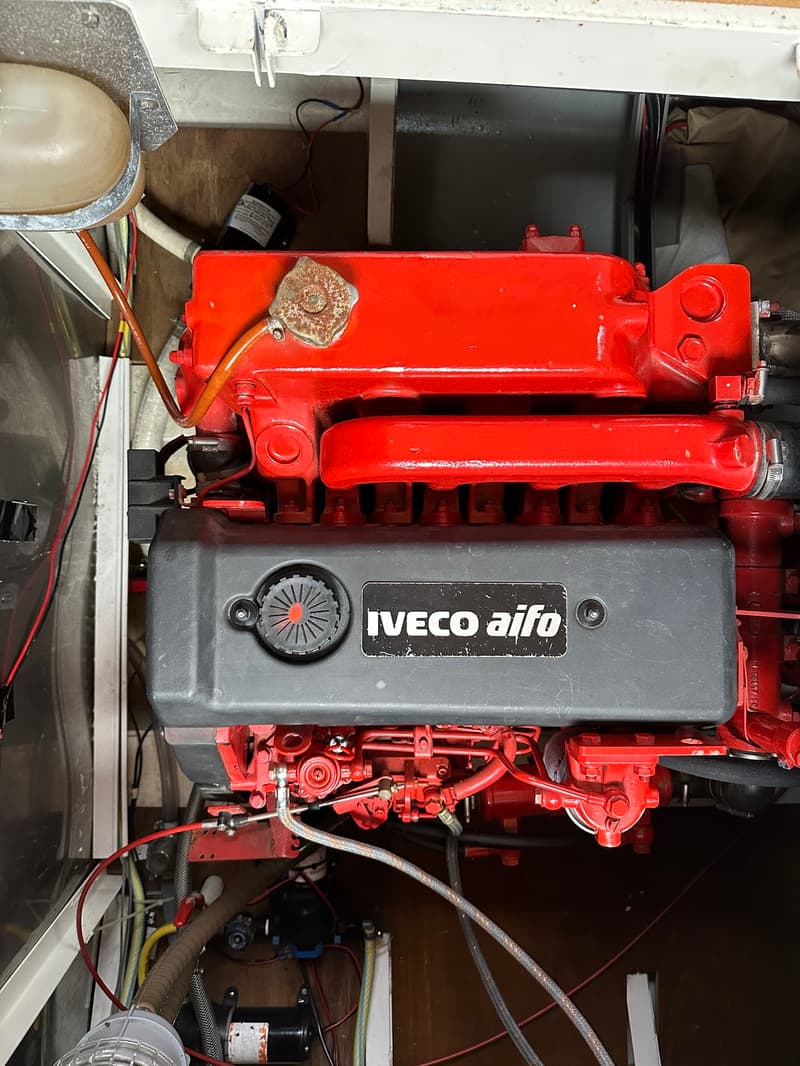 Een rode Iveco Aifo scheepsmotor met een zwarte kleppendeksel is zichtbaar, omringd door diverse slangen en bedrading.